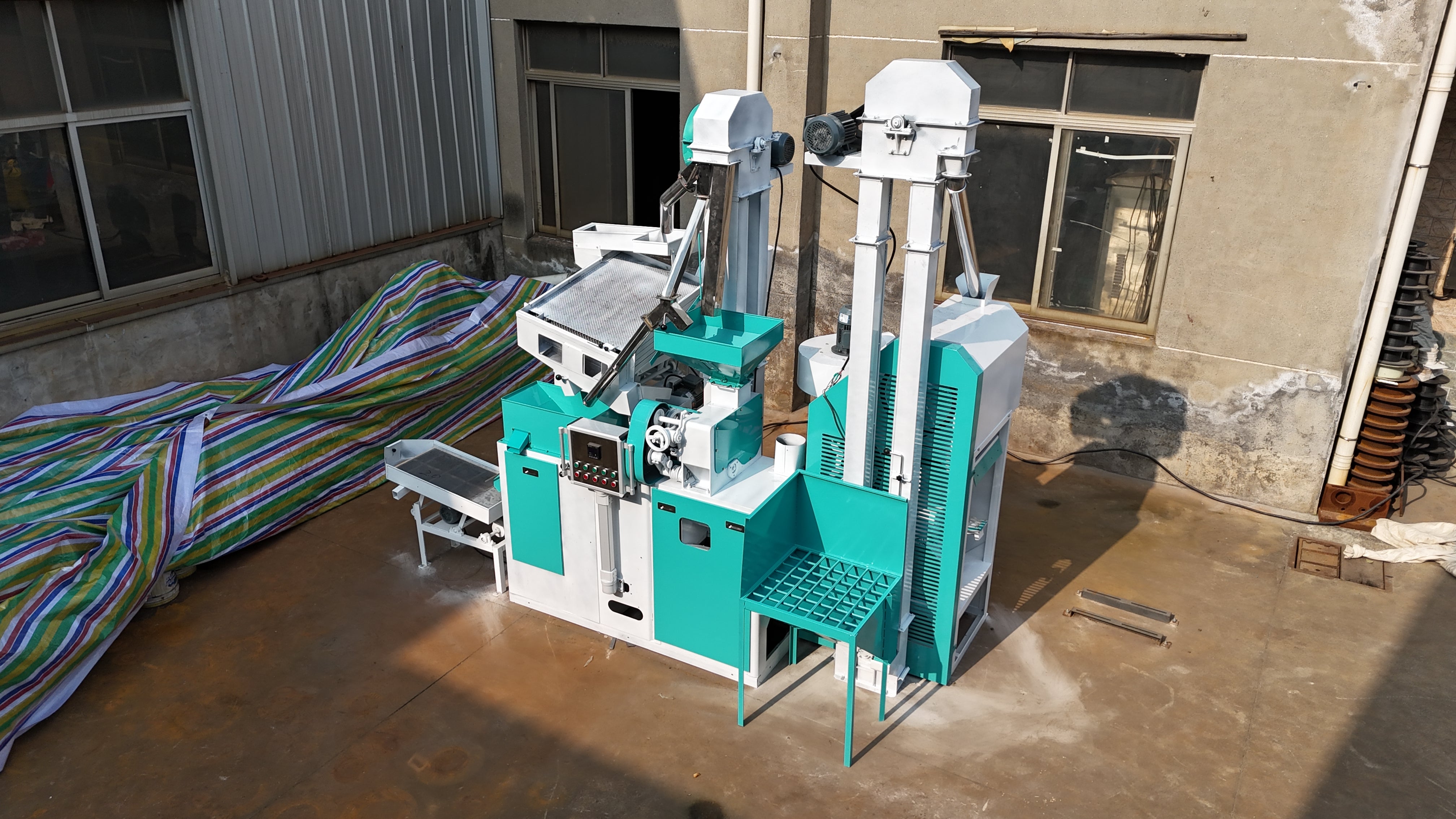 Teal and white machine on a concrete floor with a building in the background