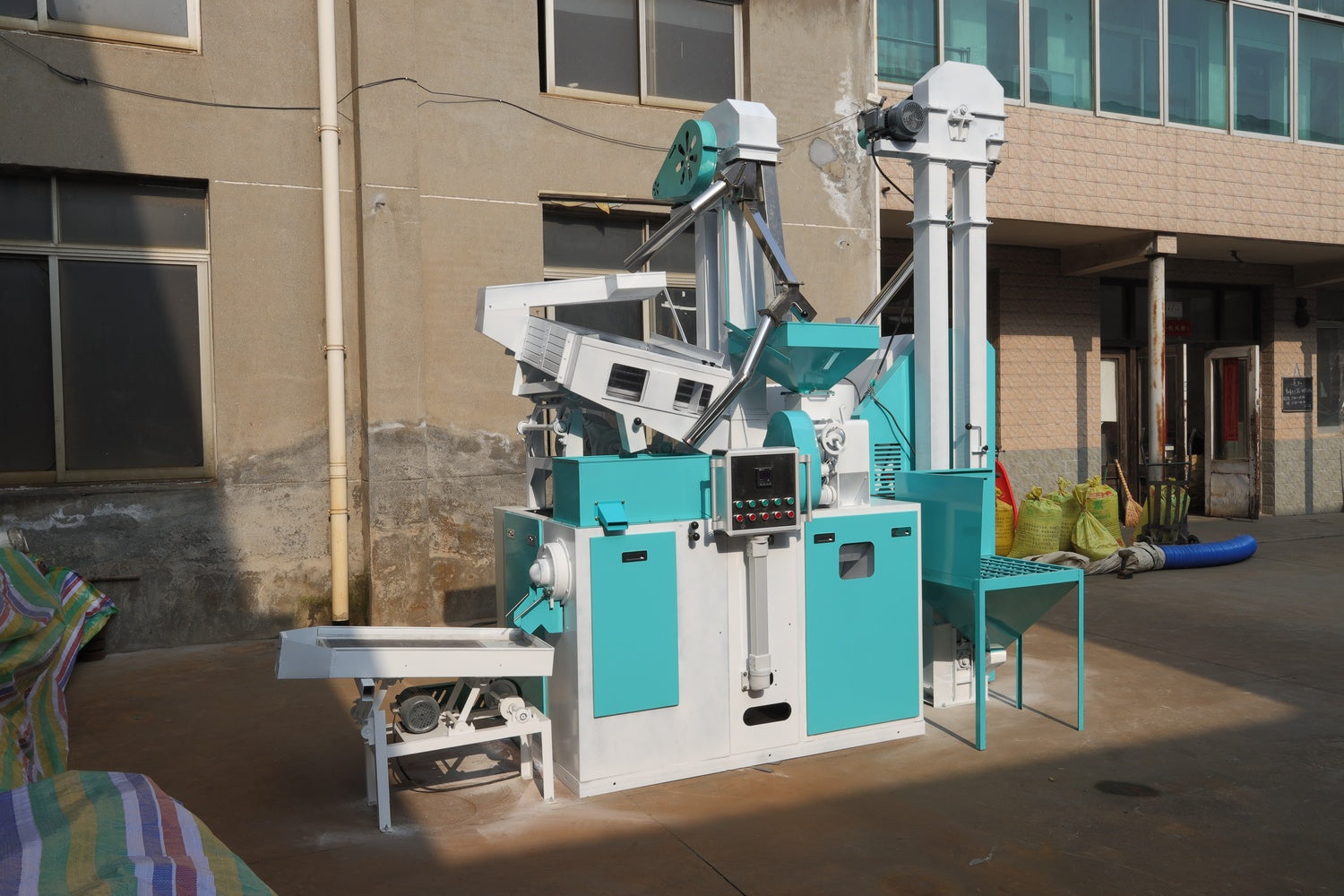 Teal and white rice processing machine in front of a building